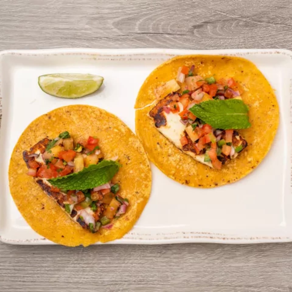 Two grilled halloumi tacos with pineapple salsa and mint, served with a lime wedge.