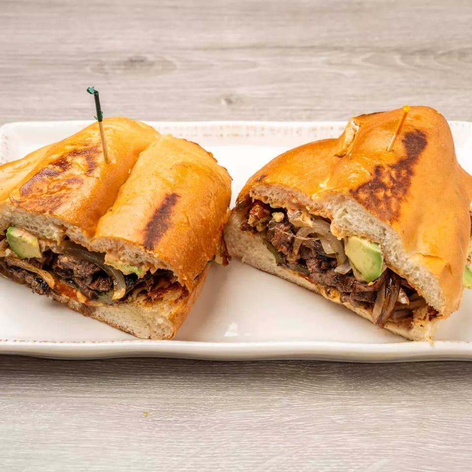 Two halves of a steak and avocado sandwich with caramelized onions on a white plate.