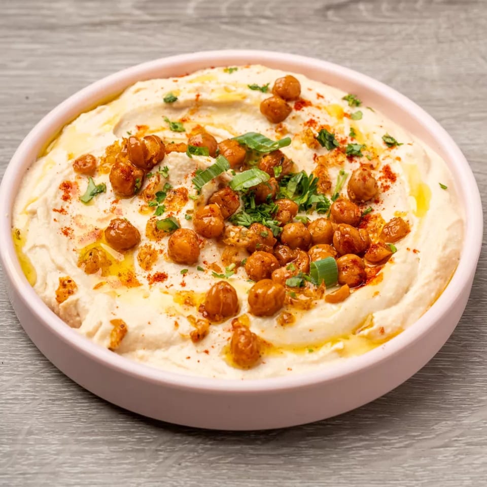Creamy hummus in a pink bowl, topped with roasted chickpeas, olive oil, paprika, and herbs.
