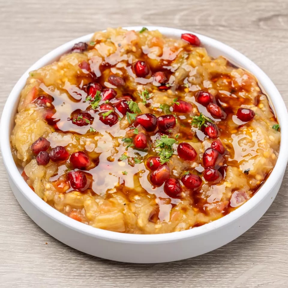 A white bowl filled with a golden-brown dish, garnished with pomegranate seeds and fresh herbs.