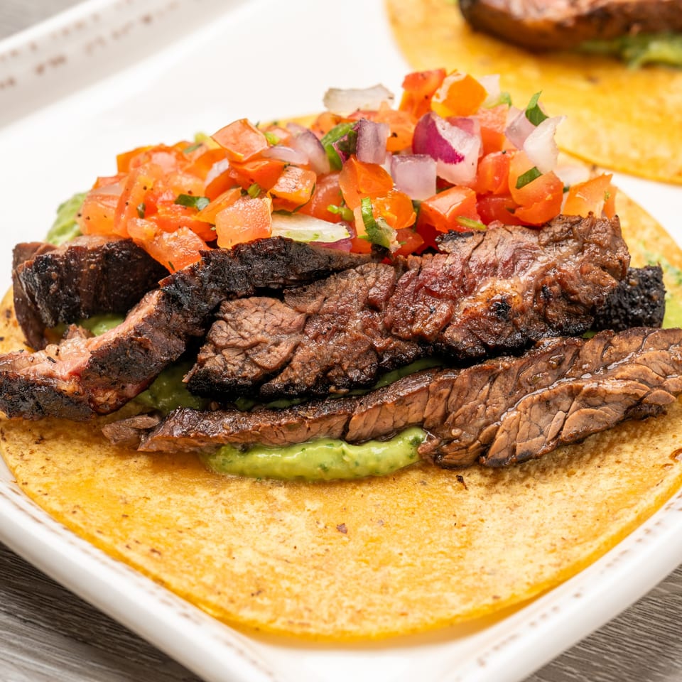 Close-up of a steak taco with guacamole and pico de gallo on a white plate.