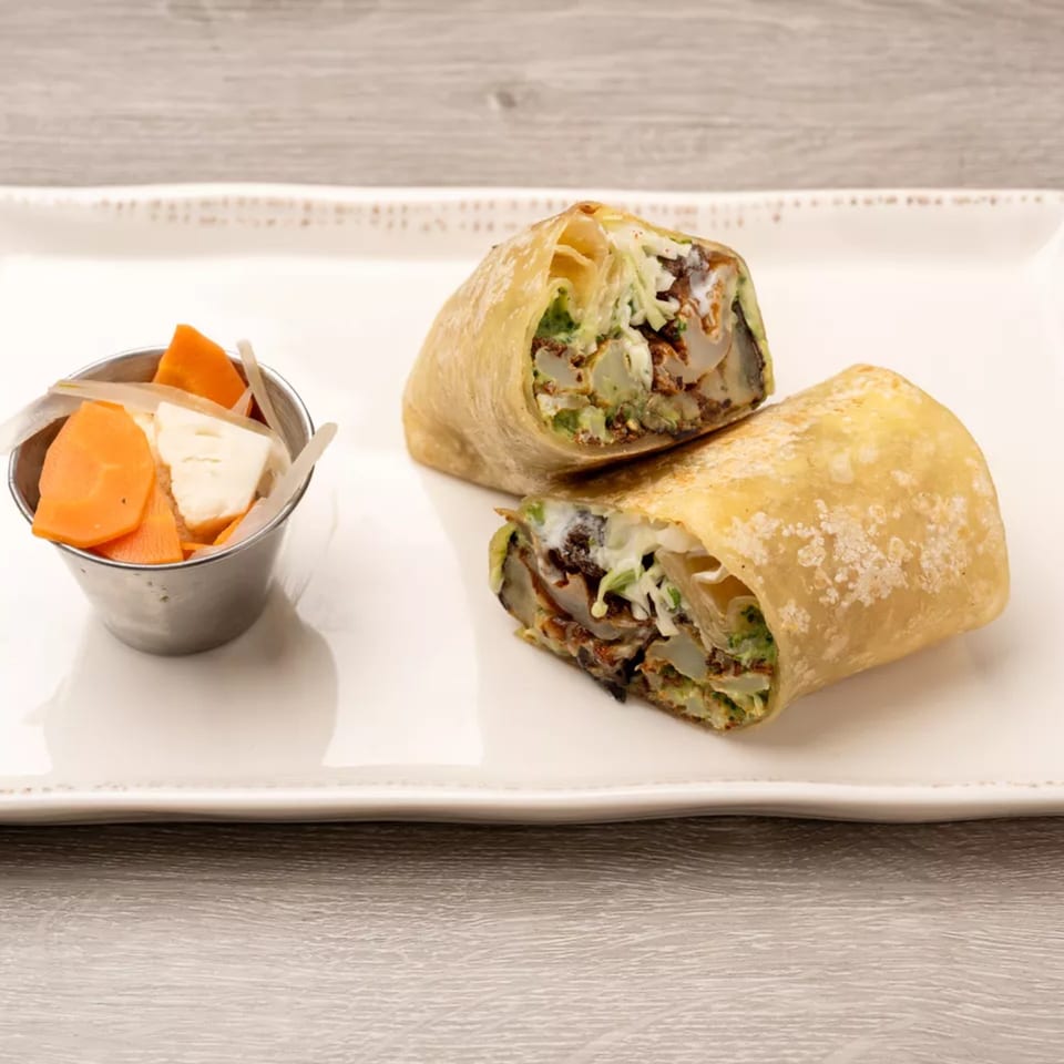 Two halves of a crispy fried burrito with green filling and a side of pickled vegetables.