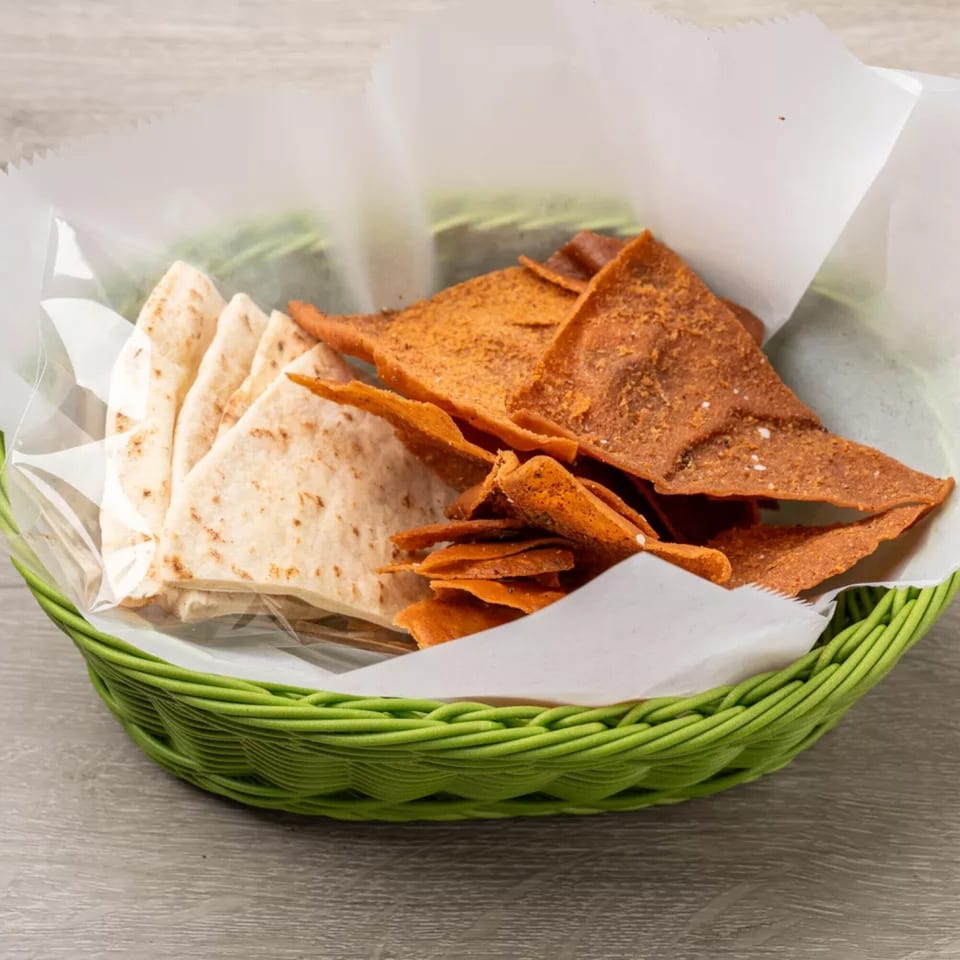 A green basket holds white pita bread and orange spiced chips, lined with white paper.