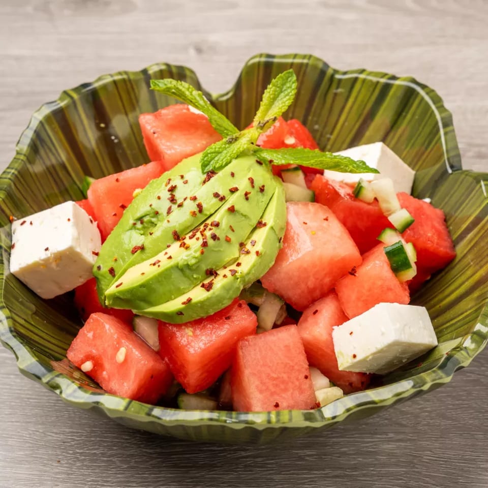 Watermelon, avocado, and feta salad with mint and spices in a green bowl.