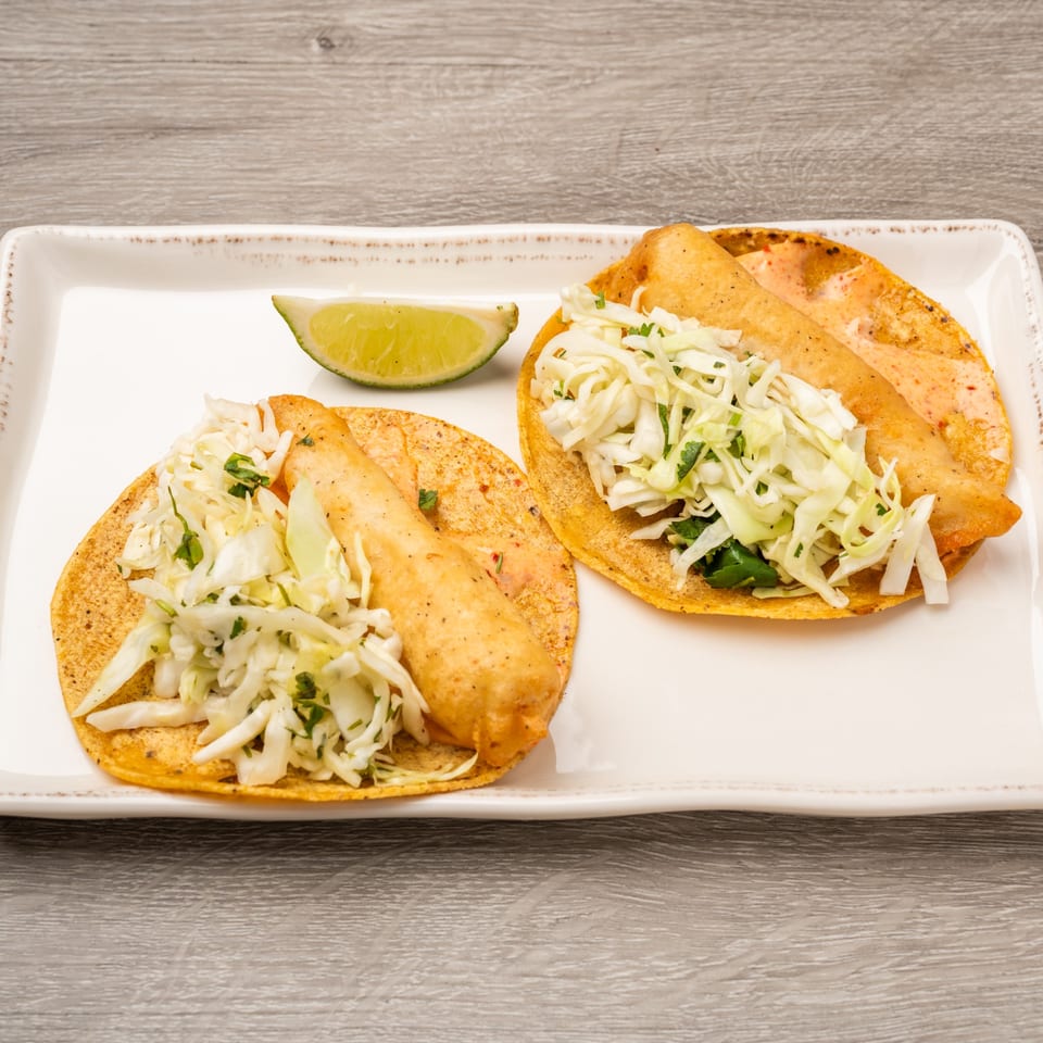 Two fish tacos with shredded cabbage and a lime wedge on a white rectangular plate.