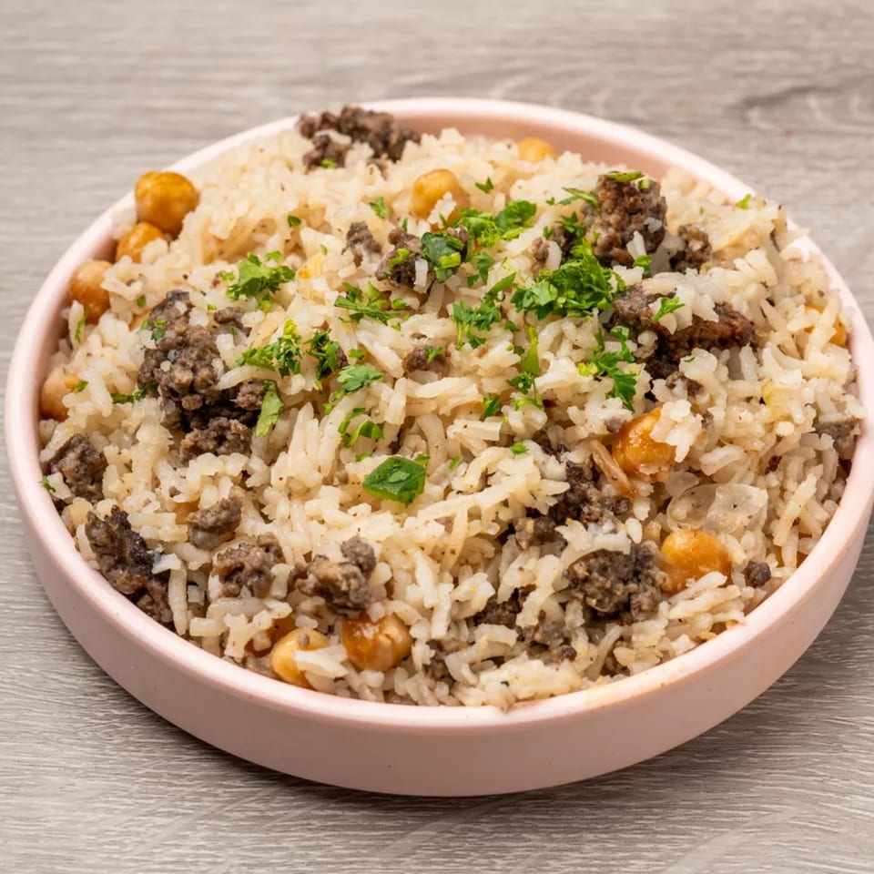 A pink bowl filled with rice, ground meat, chickpeas, and fresh parsley on a wooden table.