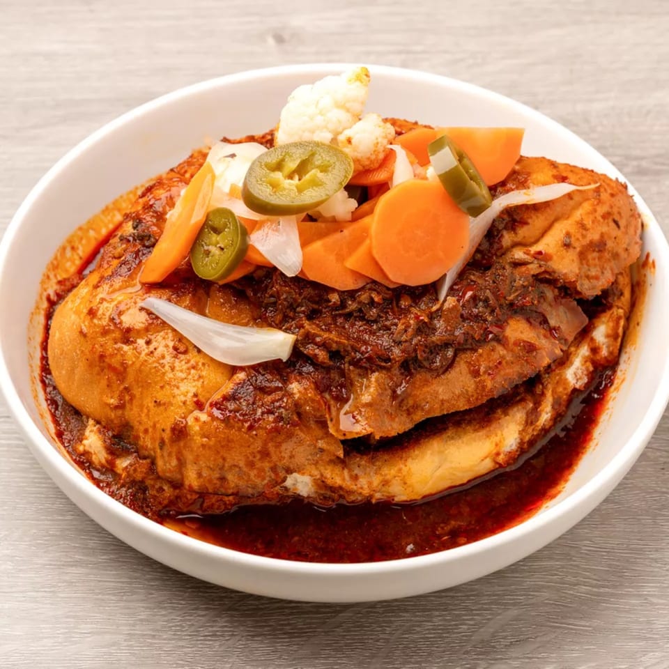 A pambazo sandwich, soaked in red sauce, topped with pickled carrots, jalapeños, onions, and cauliflower.